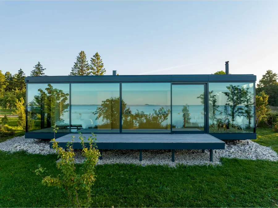 Signature glass house on a lawn above the sea, the landscape reflected in its long facade