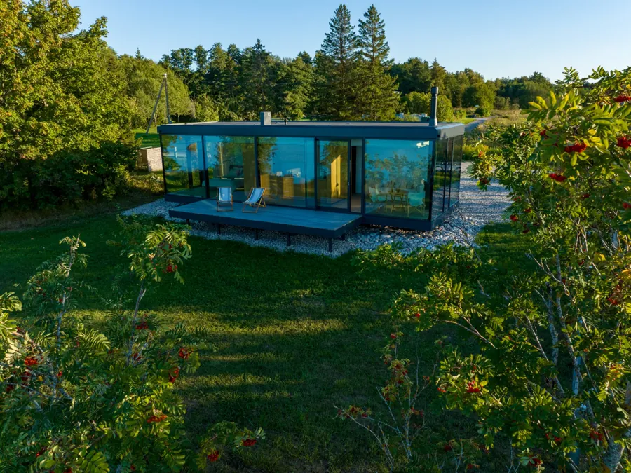 Signature glass house with a deck and two chairs on a lawn among rowan trees, seen from above