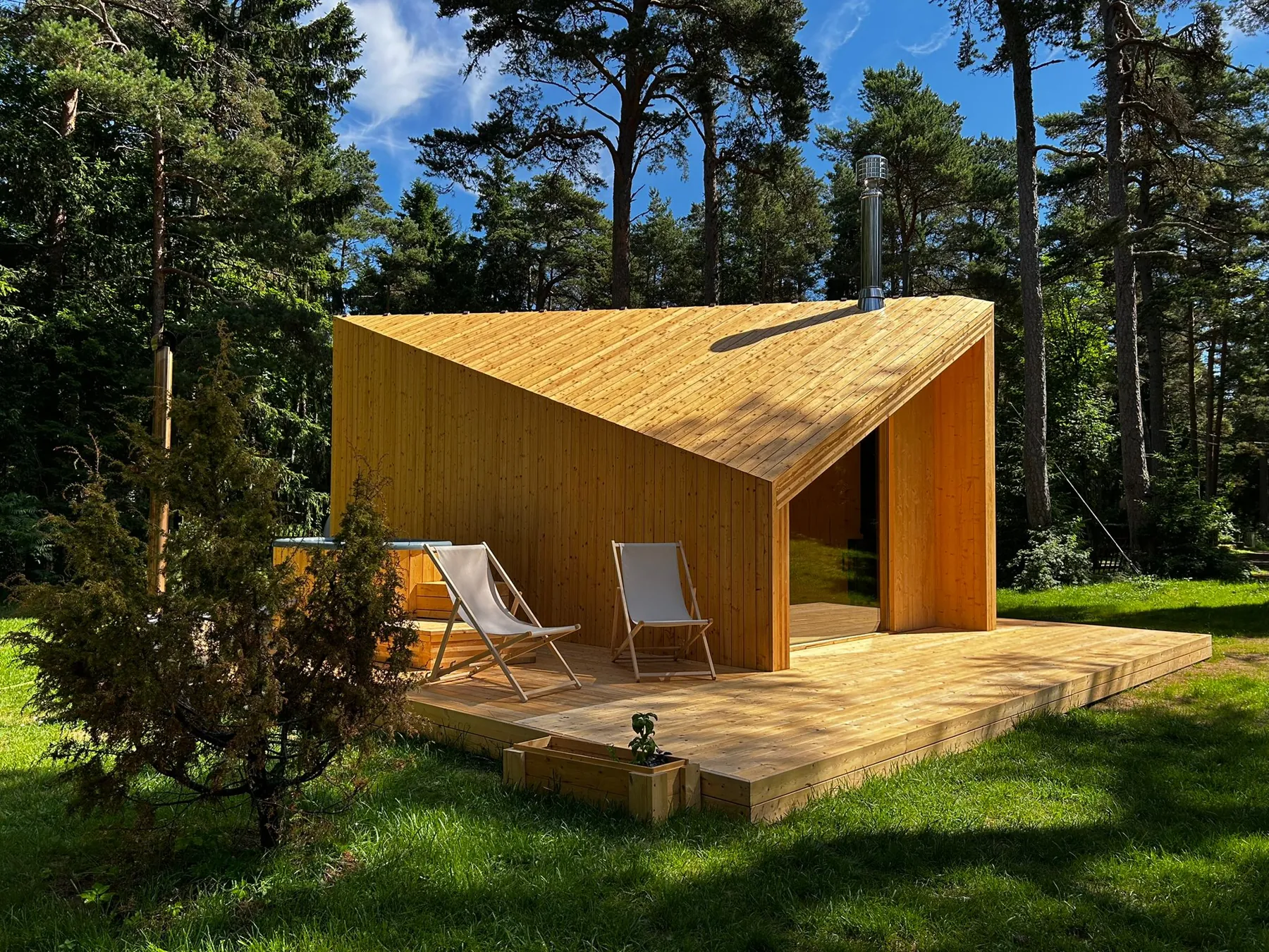 Zen cabin in pale timber under pine trees, two deck chairs on its terrace