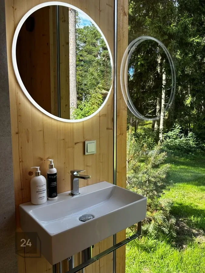 Zen bathroom with a round illuminated mirror and a full-height window onto the forest
