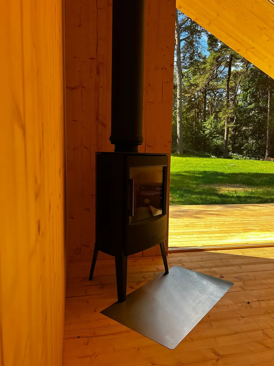 A black wood stove inside Zen, timber walls, the open door showing lawn and forest